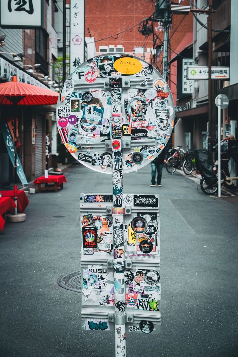 Sticker-covered sign in an urban alley with vibrant surroundings.