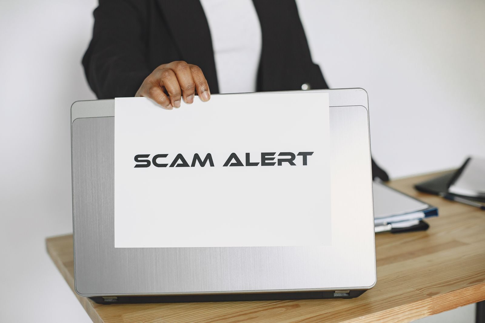 Business person holding a scam alert sign over a laptop, warning against online fraud.